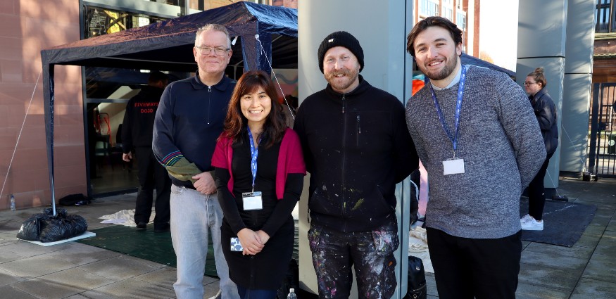 Three men and a woman smile for a photograph whilst stood in front of a gazebo.